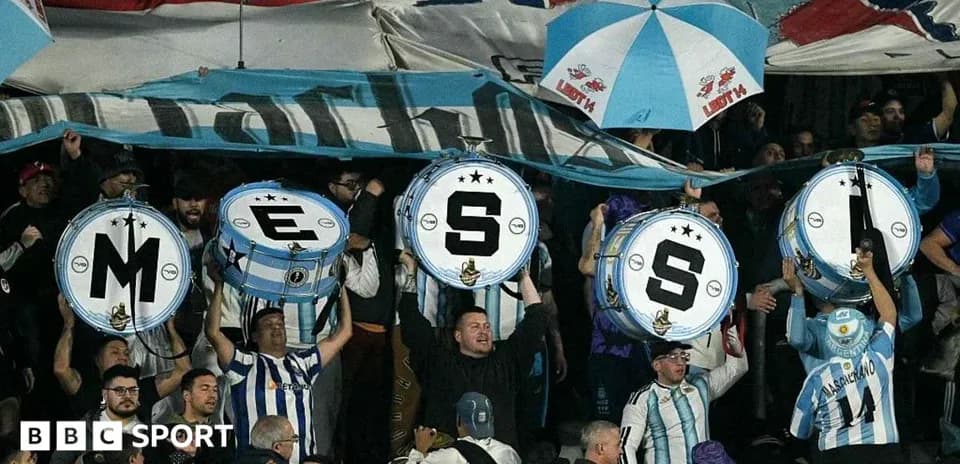 Aficionados sosteniendo tambores con letras en un estadio