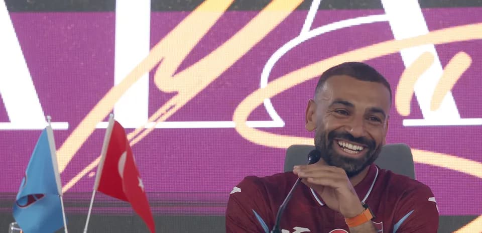 Jugador sonriente en conferencia de prensa con banderas
