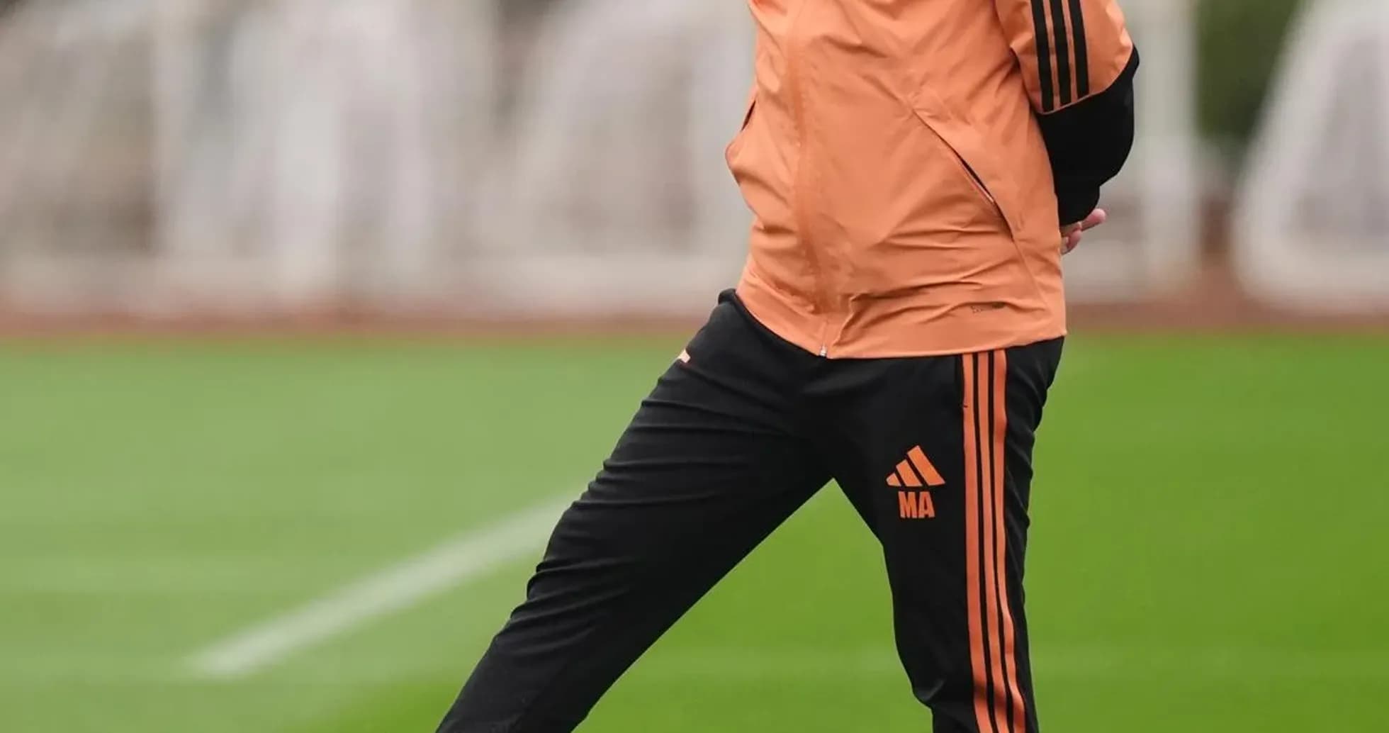 Entrenador de pie junto a balón en entrenamiento