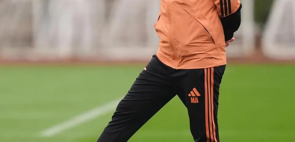 Entrenador de pie junto a balón en entrenamiento