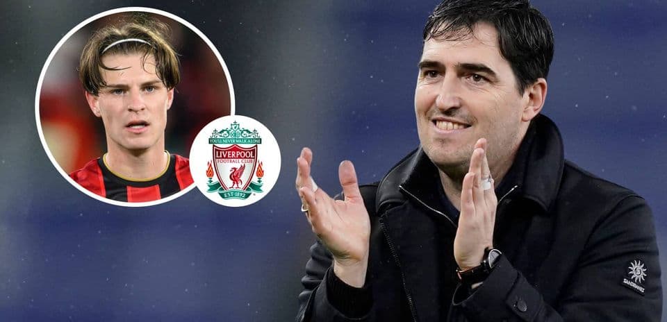 Entrenador aplaudiendo con jugador de fondo y escudo de Liverpool