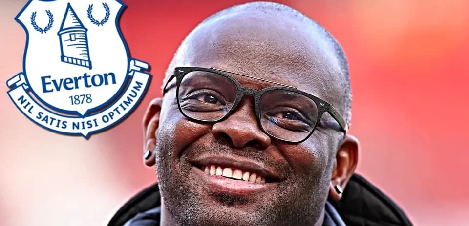 Hombre sonriendo con gafas junto al escudo de Everton