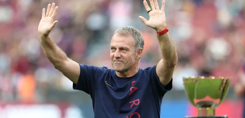 Entrenador saludando junto a trofeo en estadio