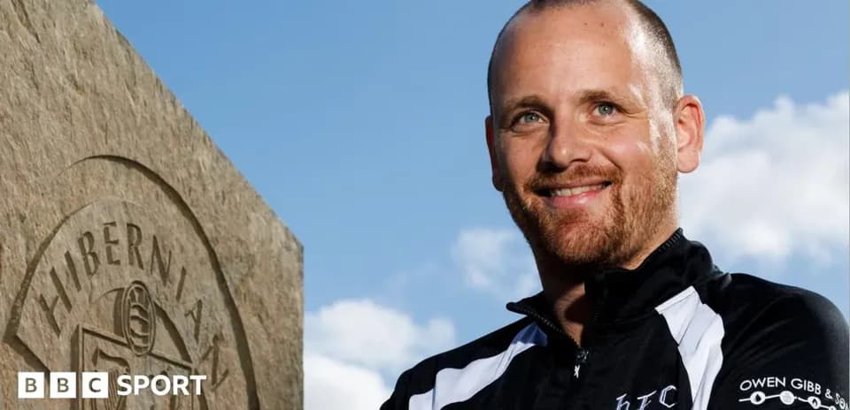 Entrenador posando junto a monumento de Hibernian