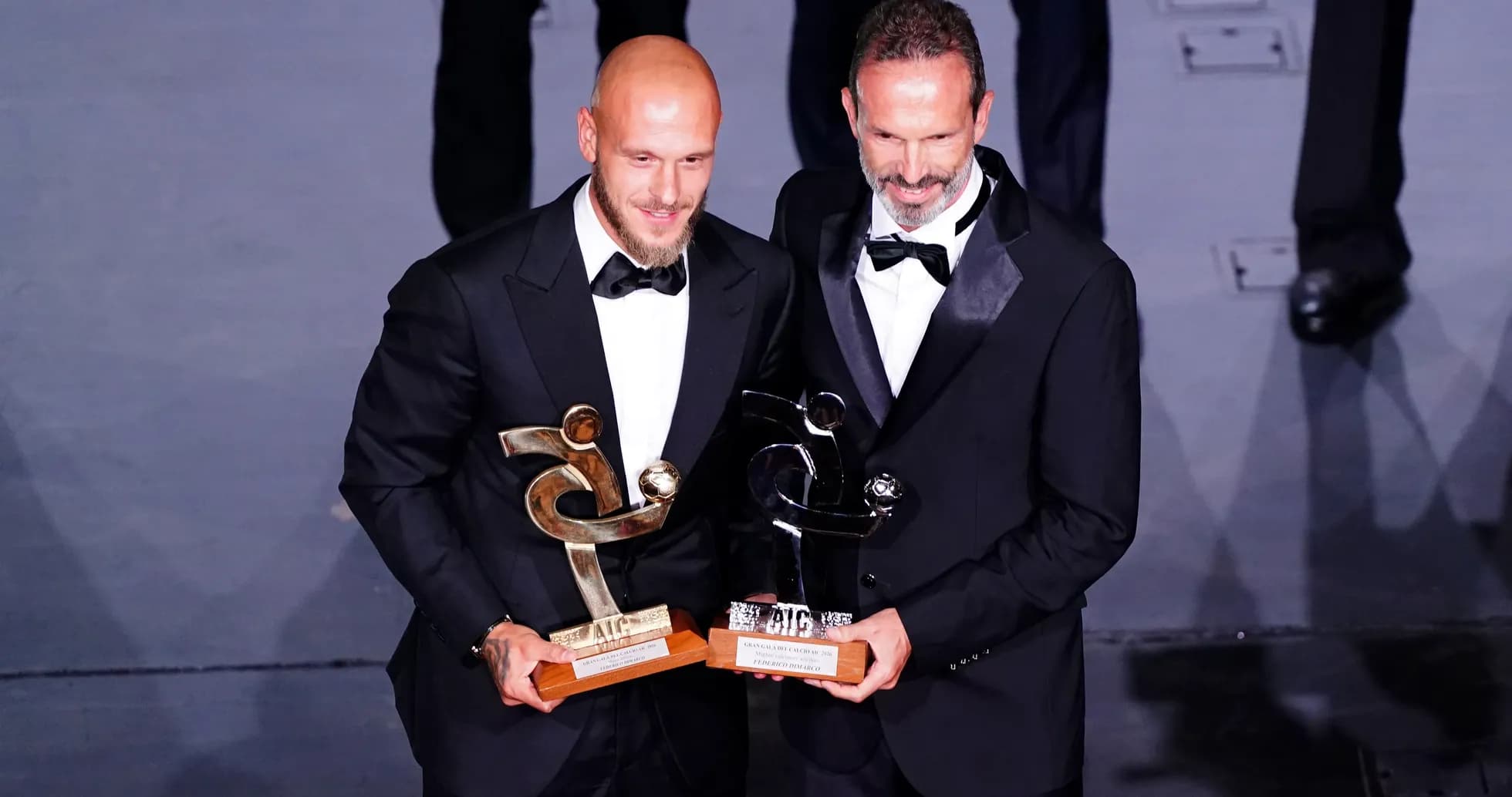 Dos hombres en traje sosteniendo premios en ceremonia
