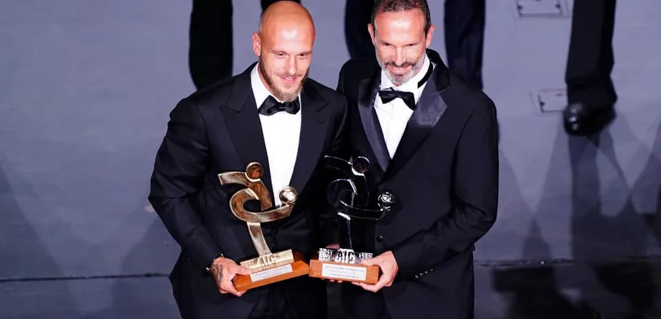 Dos hombres en traje sosteniendo premios en ceremonia