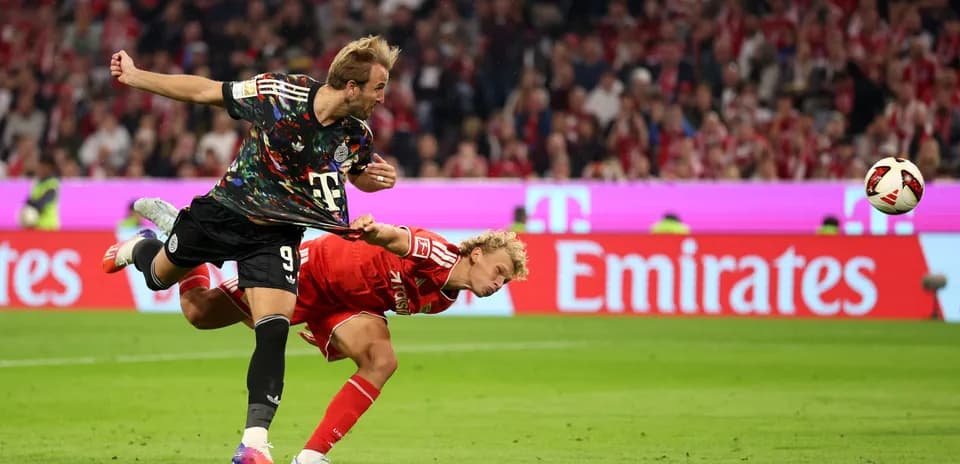 Jugador pateando el balón mientras otro cae al suelo