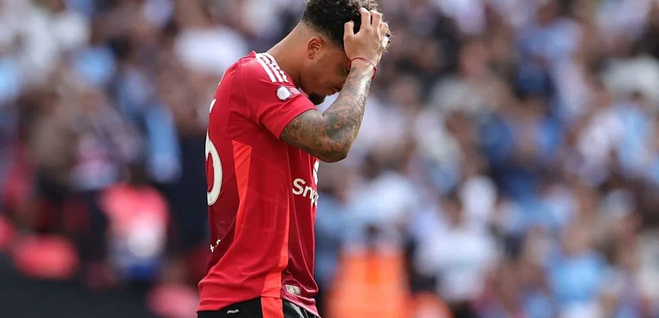 Jugador con camiseta roja sosteniendo su cabeza en el campo