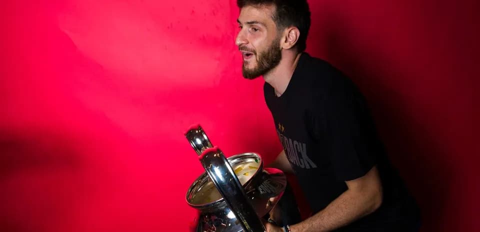 Jugador sosteniendo un trofeo frente a fondo rojo