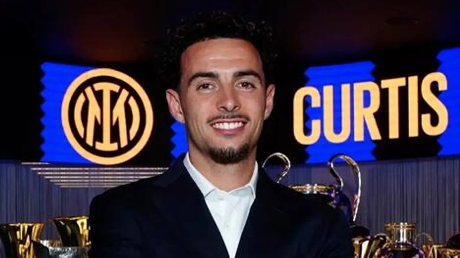 Jugador sonriente junto a trofeos y logo del club Jugador sonriente junto a trofeos y logo del club