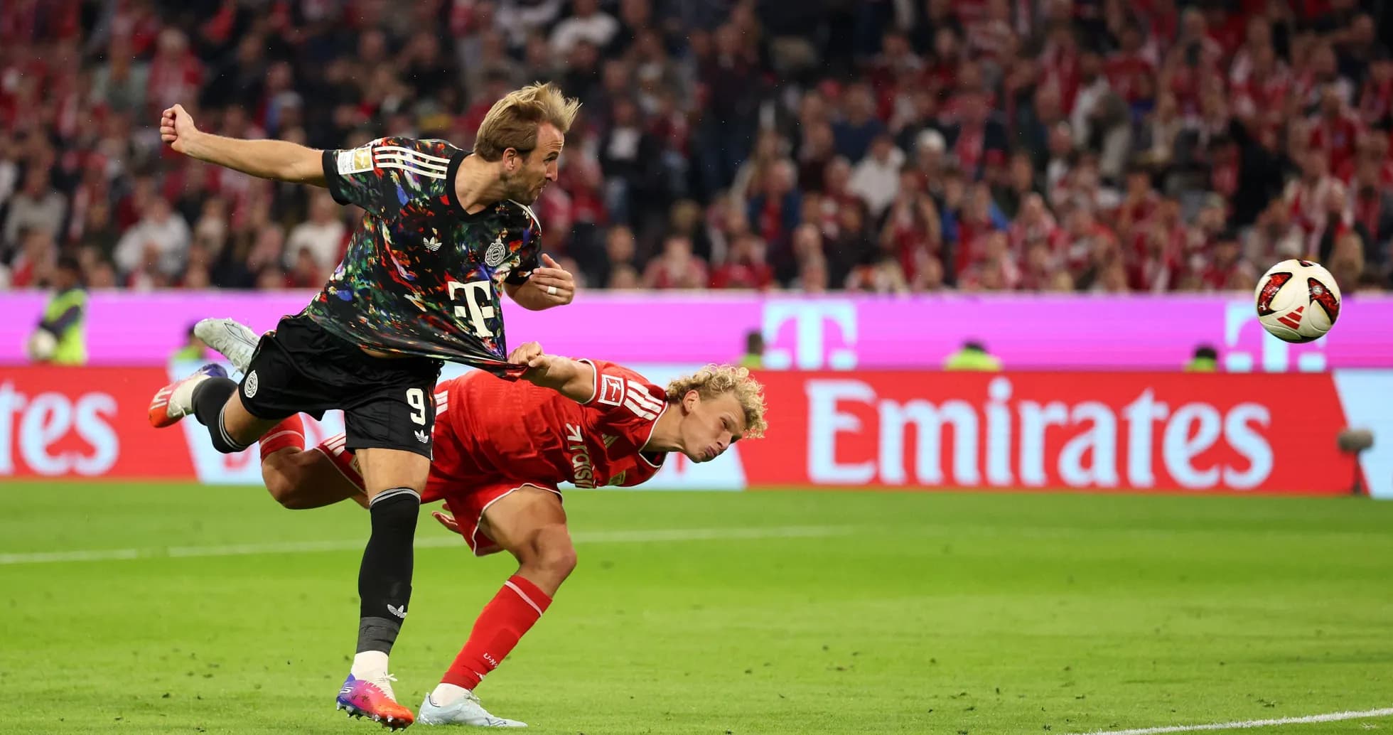 Jugador pateando el balón mientras otro cae al suelo Jugador pateando el balón mientras otro cae al suelo
