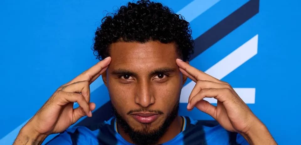 Jugador posando con fondo azul y gesto pensativo Jugador posando con fondo azul y gesto pensativo